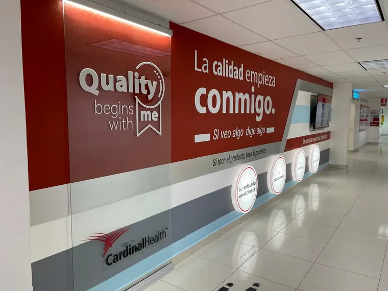 Mural corporativo de calidad con módulos iluminados, instalado en pasillo principal · Cardinal Health